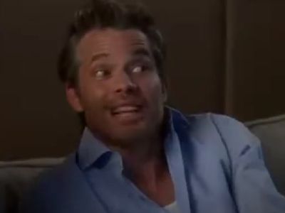 Timothy Olyphant is sitting on a sofa wearing his unbuttoned shirt.